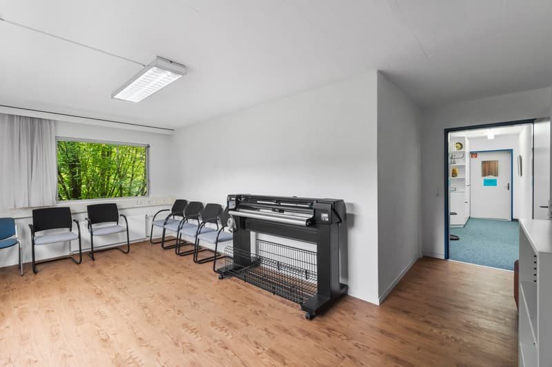 Wooden floor, white walls, ceiling light, large window with curtains, large printer/scanner in the middle, 6 blue chairs