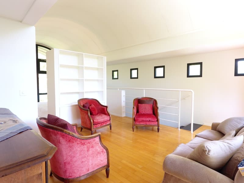 Wooden floor, white walls, a large couch, 3 armchairs, a white bookshelf