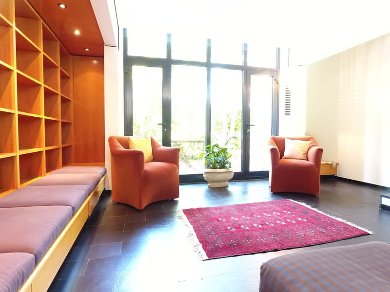 living room with 2 orange armchairs, wooden sofa, and a plant, large windows, wooden bench, red rug