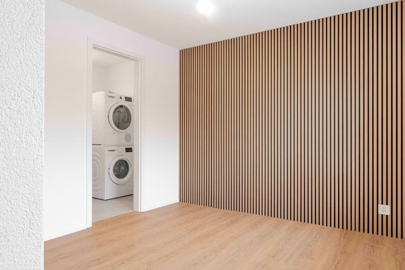 empty room with wooden floor, white walls, wooden wall paneling, two white washing machines