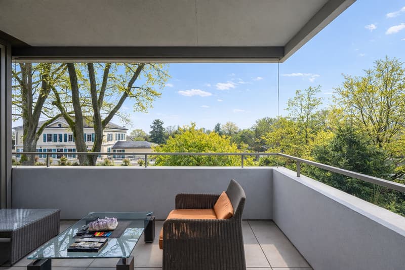 Balcony with seating, railing, concrete flooring, glass table, clear sky