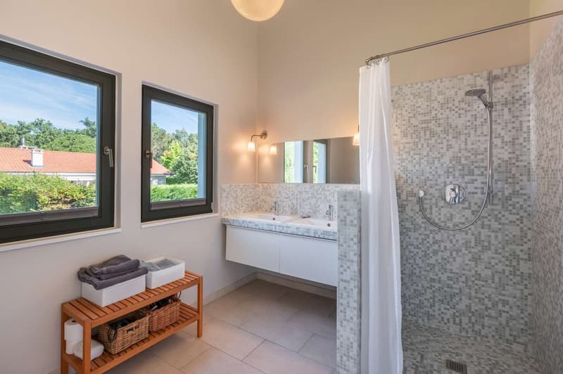 Spacious bathroom with large windows, mosaic tile walls, vanity with sink, shower with curtain, and a wooden storage rack