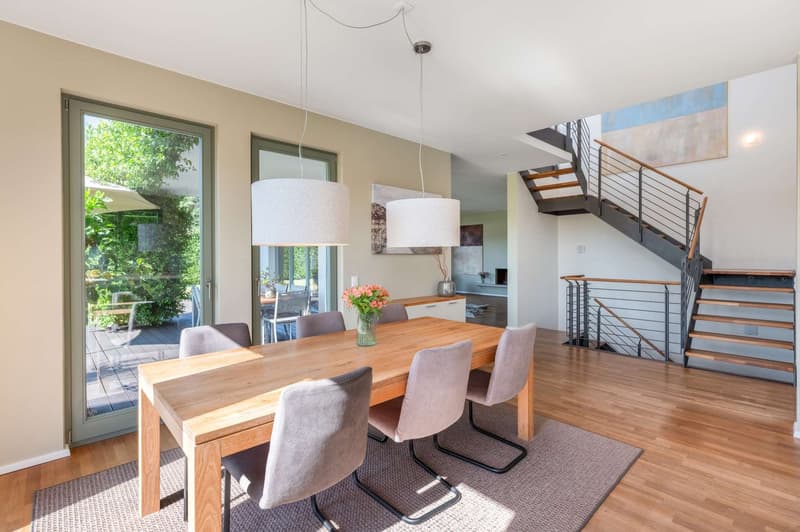 wooden dining table, cushioned chairs, large sliding glass door leading to balcony with greenery view
