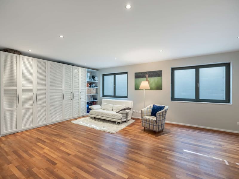 Spacious living room with hardwood flooring, white built-in cabinets/closets, large windows, a white sofa, and a plaid armchair.
