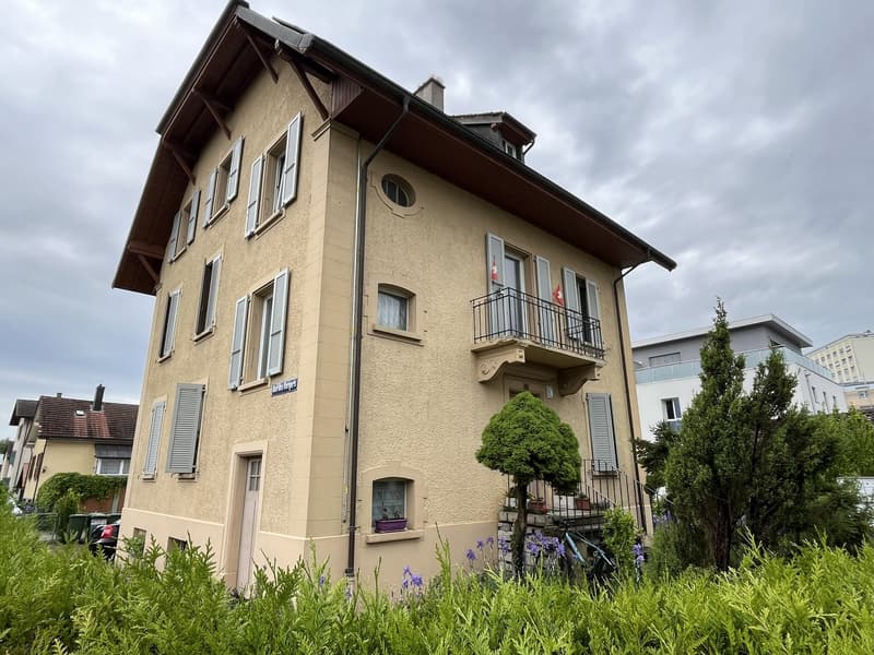 3 story apartment, beige facade, multiple windows, balcony, shrubs, flag