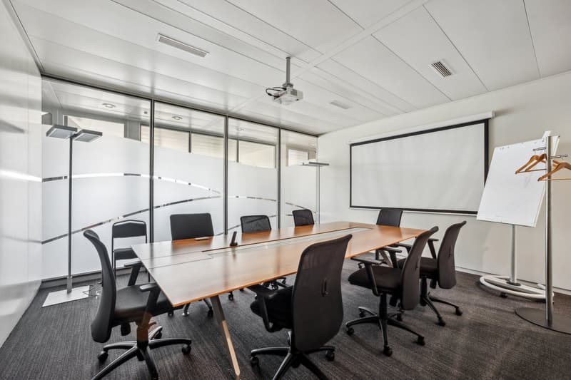 modern meeting room with a long wooden table, black chairs, a white screen, a projector, a whiteboard, and a projector stand