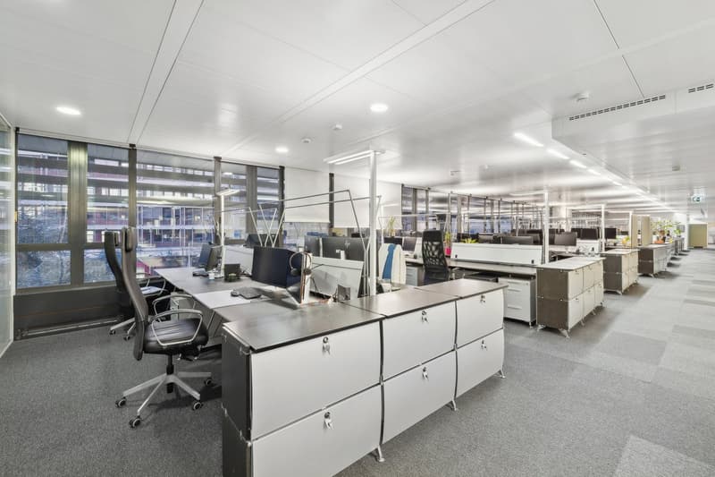 modern office with desks, computer screens, chairs, lamps, carpeted floor, large windows, modern design
