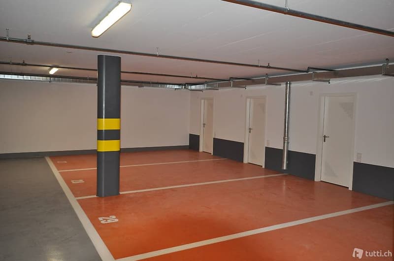 Empty basement floor, multiple parking bays, white and grey walls, gray floor, fluorescent lights