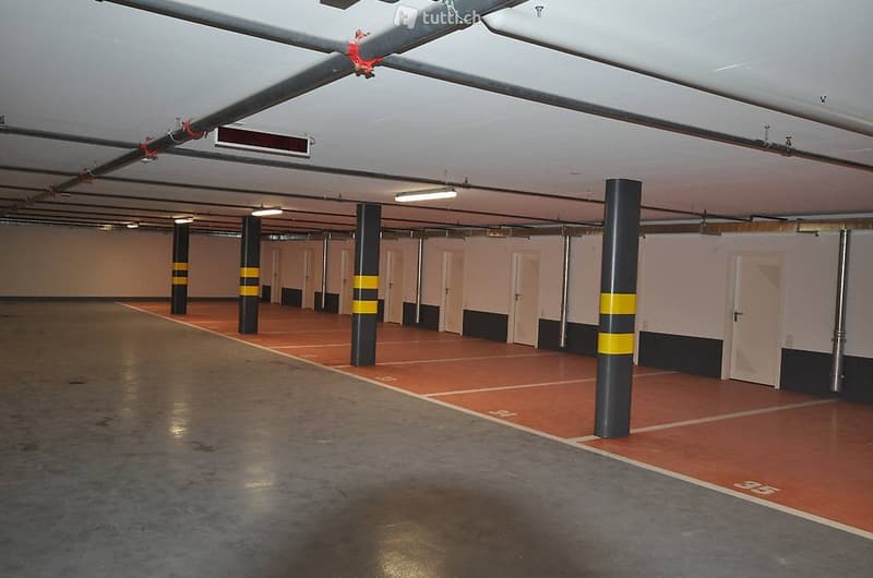Empty parking lot with white walls, black and yellow columns, numbered parking spaces, fluorescent lighting