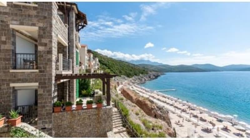 Multi-story apartment building with stone exterior, balconies, and a scenic view of the coastline and mountains in the background.