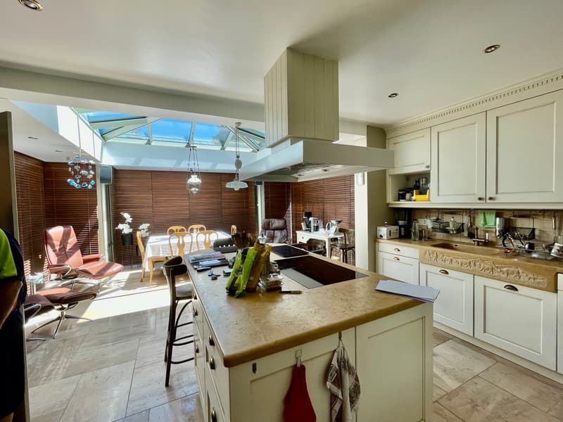 modern kitchen with center island, ceiling lamps, dining area with glass table, wooden blinds, white cupboards
