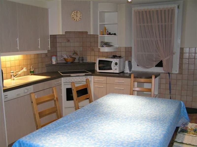 Modern kitchen with a dining area, stove, microwave, sink, dishwasher, wooden chairs, tile flooring