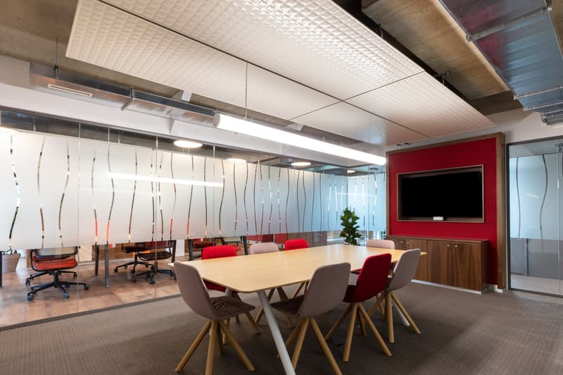 Large open office space with a conference table, red accent wall, glass partitions, and modern furniture