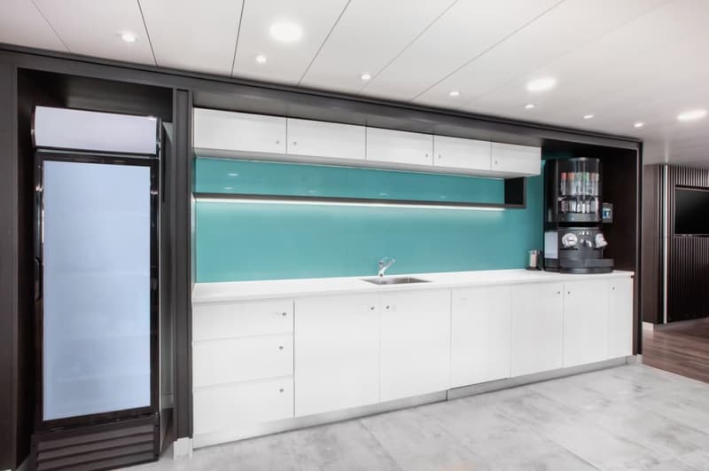 Modern, open-concept kitchen with white cabinets, teal backsplash, stainless steel appliances including a dishwasher, and large windows providing natural light