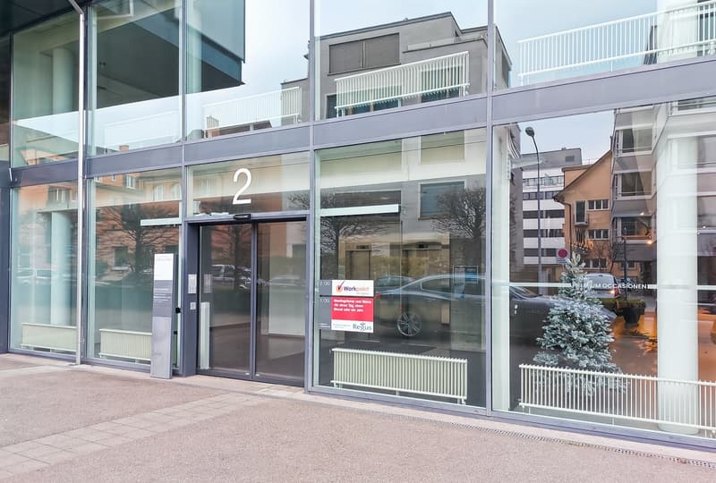 2-story commercial building with glass facade, entrance doors, and signage for 'Workpoint' and 'Regus' businesses. There is a parked car visible in front of the building and a small tree in the foreground.