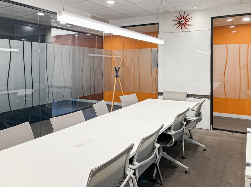 Modern office space with a large white conference table, gray chairs, glass partitions, and a red star-shaped light fixture on the wall.