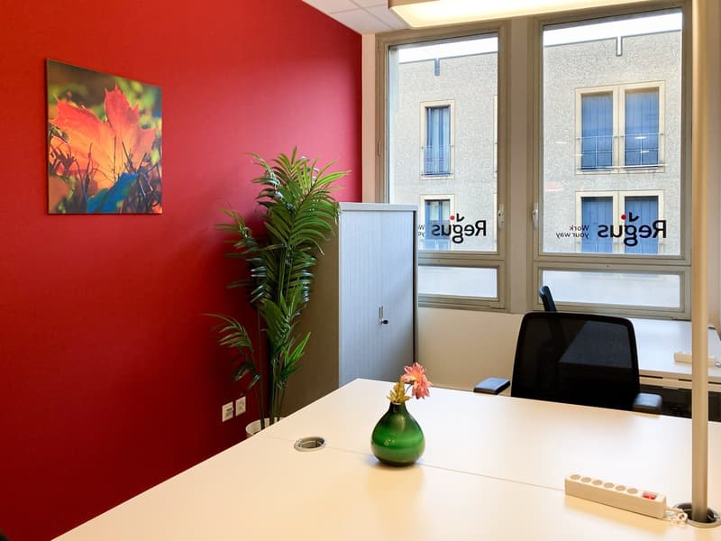 Red accent wall, large windows, potted plant, artwork, desk with computer, office supplies