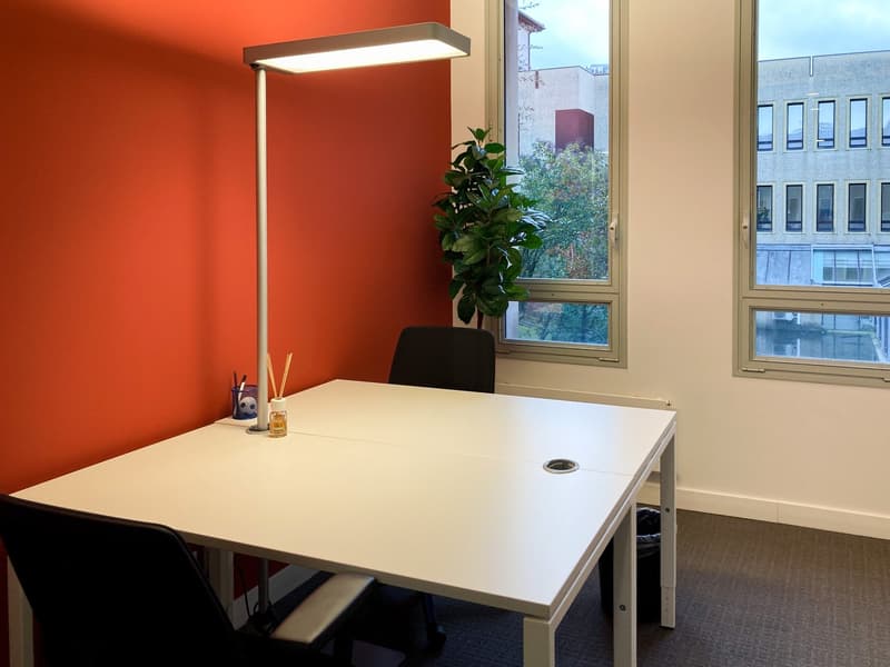 Bright office space with large windows, white desk, black chair, potted plant, and desk lamp