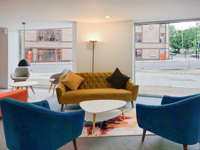 yellow tufted couch, blue accent chairs, white coffee table, rug, floor lamp, glass walls, bollards outside