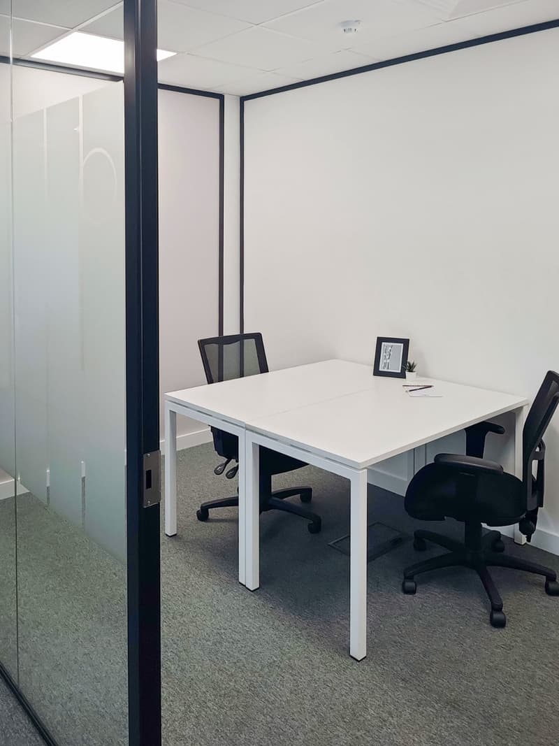 Glass partition, white desk, two black swivel chairs, picture frame with a plant, writing utensils