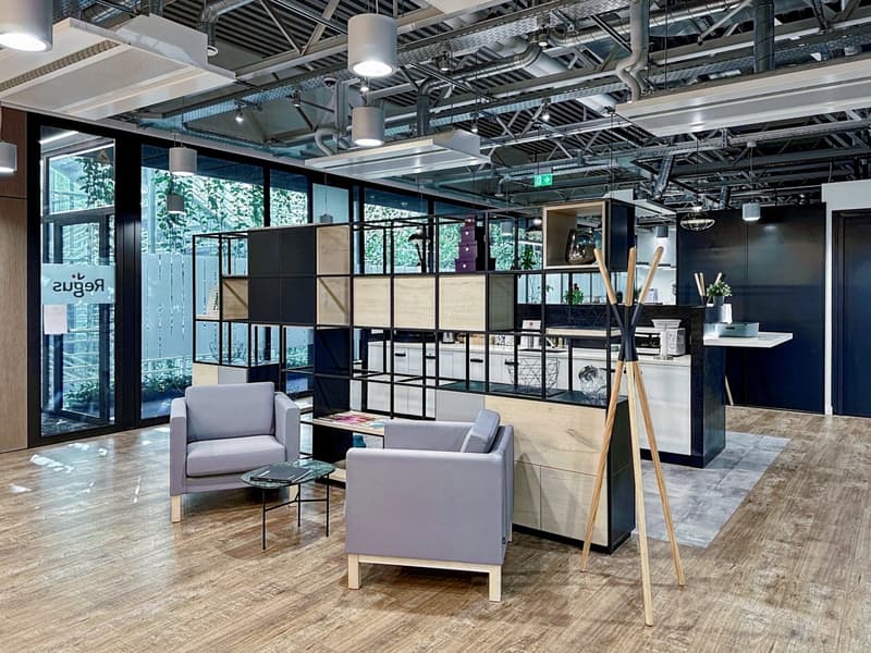 modern office with wooden floors, glass walls, seating area with two chairs and a table, modern furniture with cabinets and shelves, lamps, and metal stand