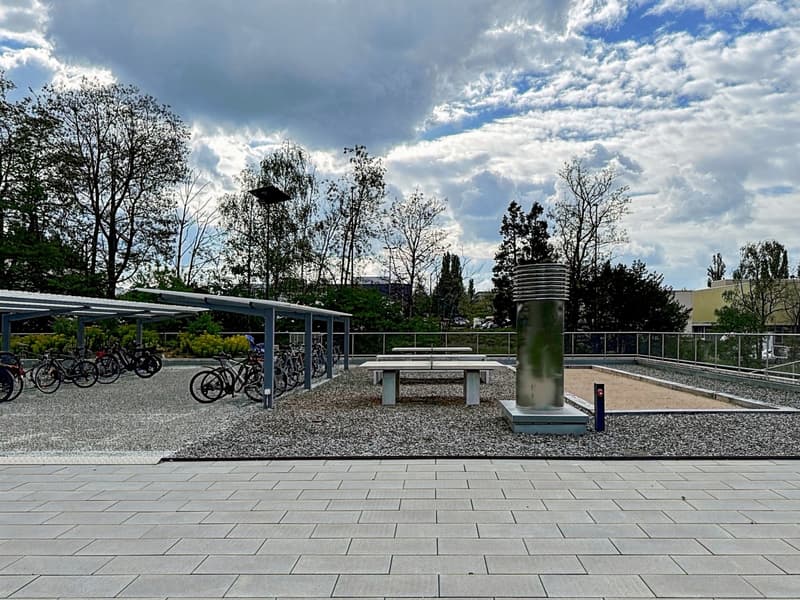 paved area, table tennis table, bicycles under shelter, gravel ground, trees, metal railings