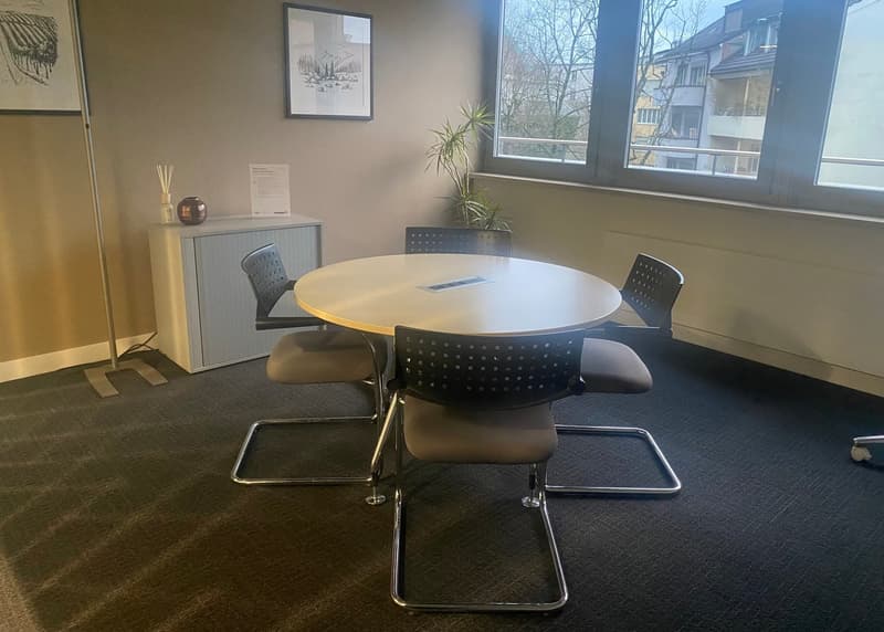 empty meeting room with round table, 4 chairs, cabinet, 2 picture frames, plant, windows