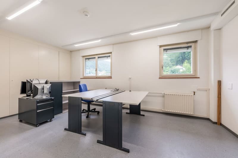 two white desks, computer monitors, a blue office chair, office cabinets, radiators