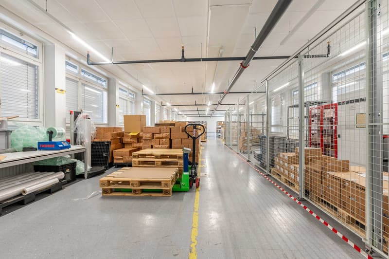 Warehouse with stacks of boxes, forklift, long aisle, cages, windows, grey floor