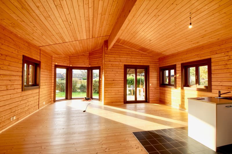 wooden walls, wooden floor, large windows, kitchen area with sink and faucet