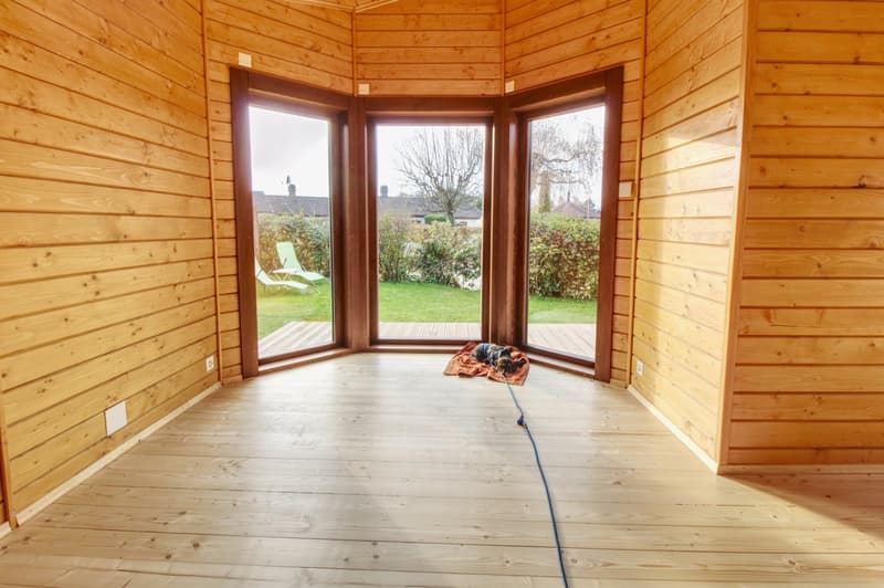wooden walls, wooden floor, large windows, balcony, outdoor area with grass and chairs