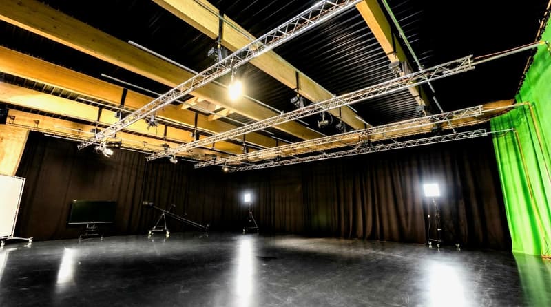 Empty room with black floor, wooden ceiling, black curtains, green screen, lighting equipment