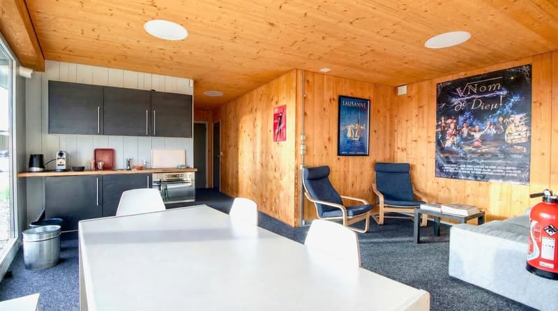 Dining area with a table, chairs, and a couch. There is a kitchen area with cabinets, a stove, and a coffee machine. There is a poster on the wall.