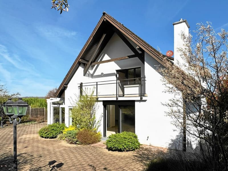 white house, brown roof, balcony, brick driveway, fenced garden