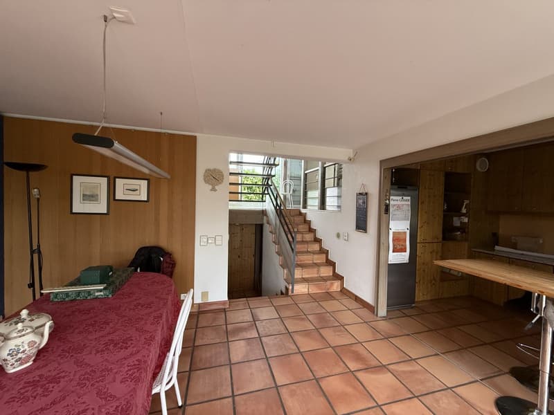 main room with stairs leading up, red tablecloth, chair, table with teapot, lamp, wood floor, two picture frames, staircase
