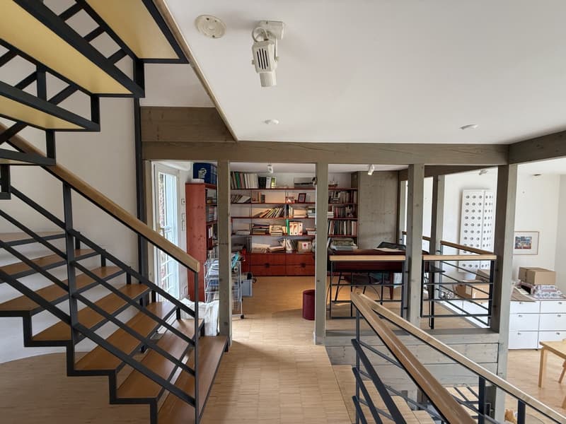 Interior of a house with a staircase, wooden floor, white walls, a bookshelf, desk, and a modern design.