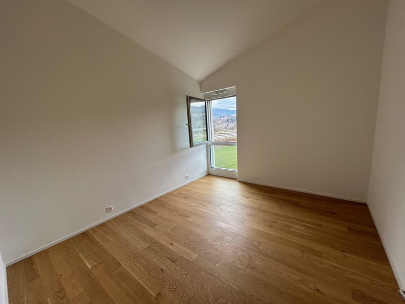 Spacious bedroom with hardwood flooring, neutral-colored walls, and a large window providing a scenic view of the surrounding landscape.