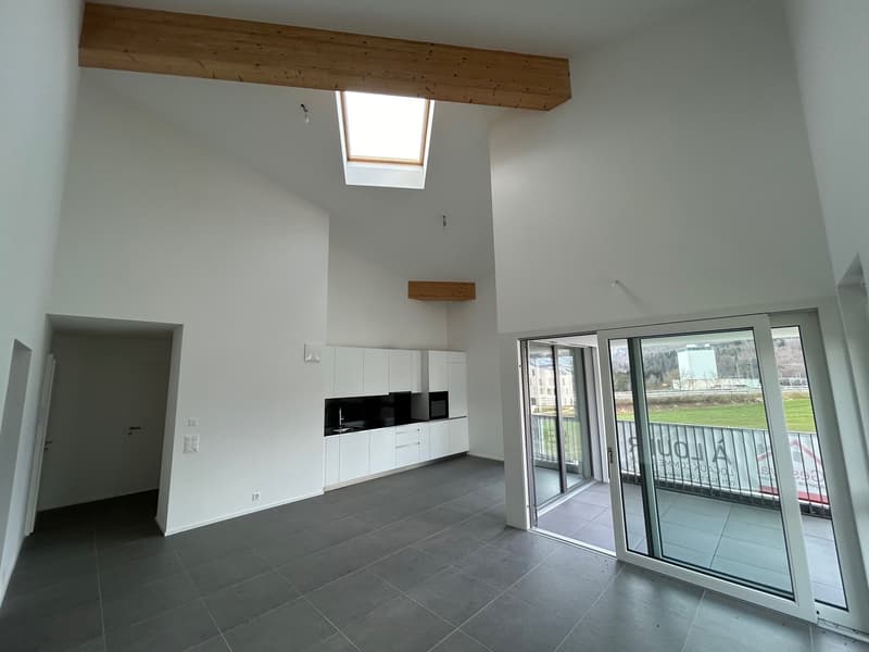 Open-concept living space with high ceilings, wooden beams, large windows, sliding glass doors leading to a balcony, and a modern kitchen with white cabinets and black appliances
