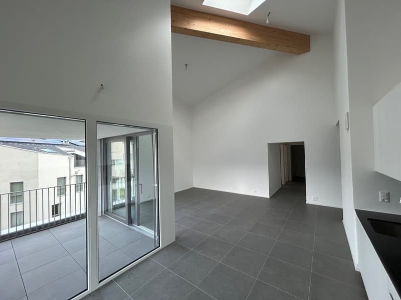 Spacious open-plan living area with large sliding glass doors leading to a balcony or terrace, hardwood ceiling beams, and gray tile flooring.