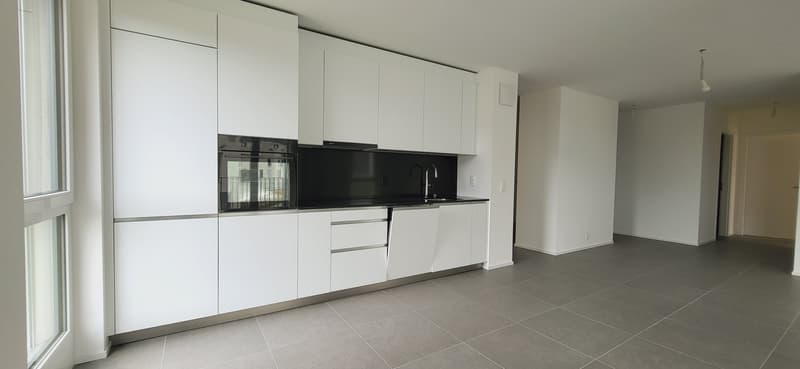 Modern, open-concept kitchen with white cabinets, black countertops, built-in oven and dishwasher, and tile flooring