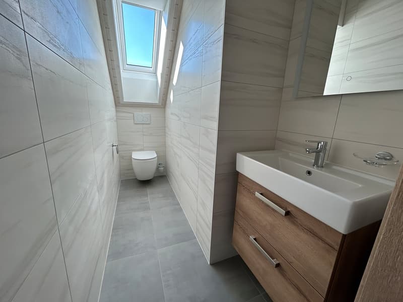 modern bathroom with white tile walls, white sink, white toilet, wooden cabinet, and skylight window