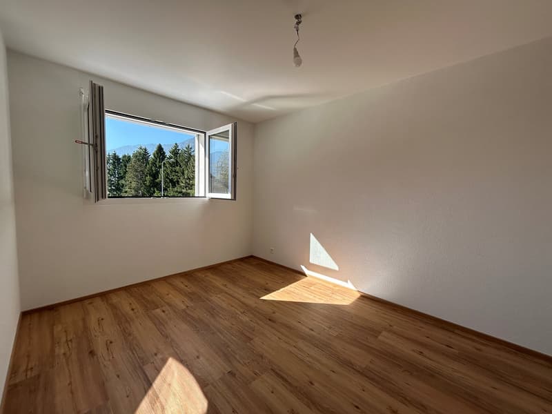 Empty room with hardwood floors, white walls, open window with trees view, pendant light