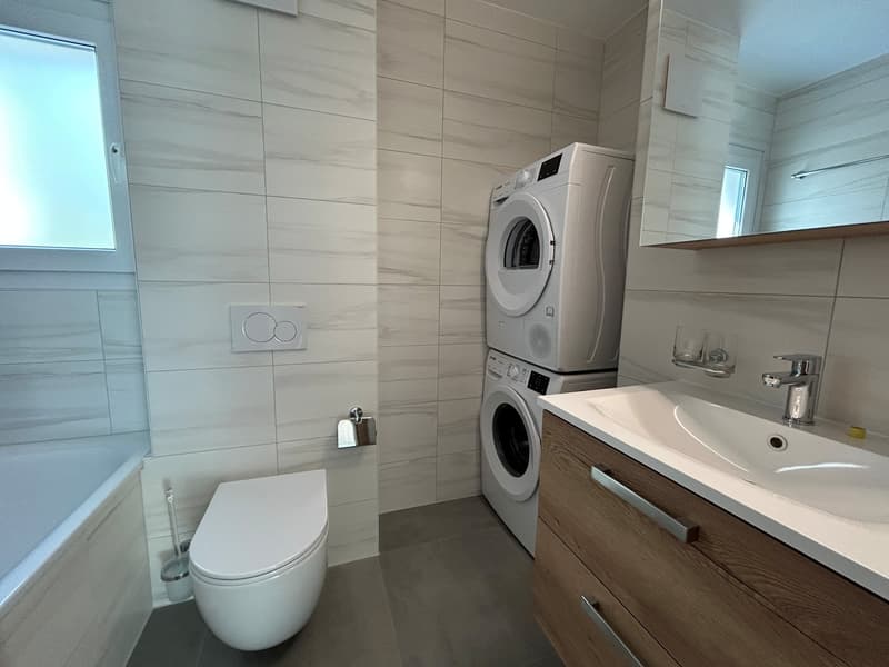 a compact bathroom with a bathtub, toilet, and washing machine under the sink