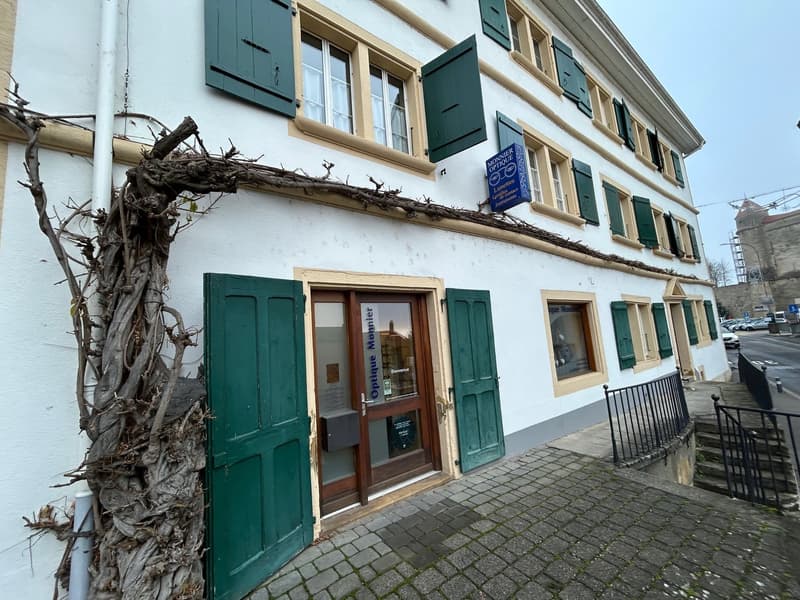 3-story white building with green shutters, a signboard, and vines growing around the front entrance