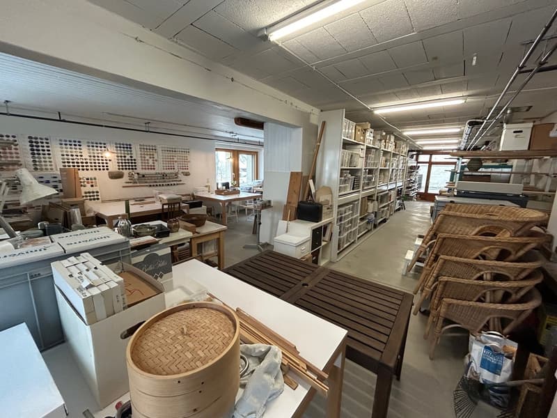 Room with tables, shelves, baskets, a wicker chair, storage boxes, ceiling lights
