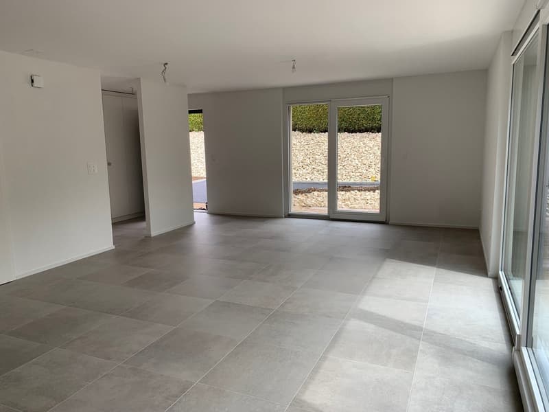 Empty room, white tiles, sliding glass door leading to terrace, large windows