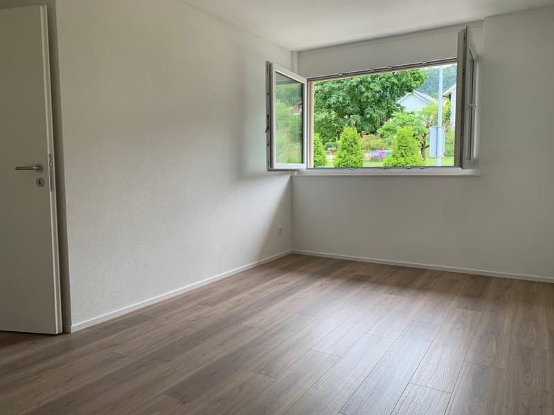 empty room with wooden floors, white walls, open window with view of trees