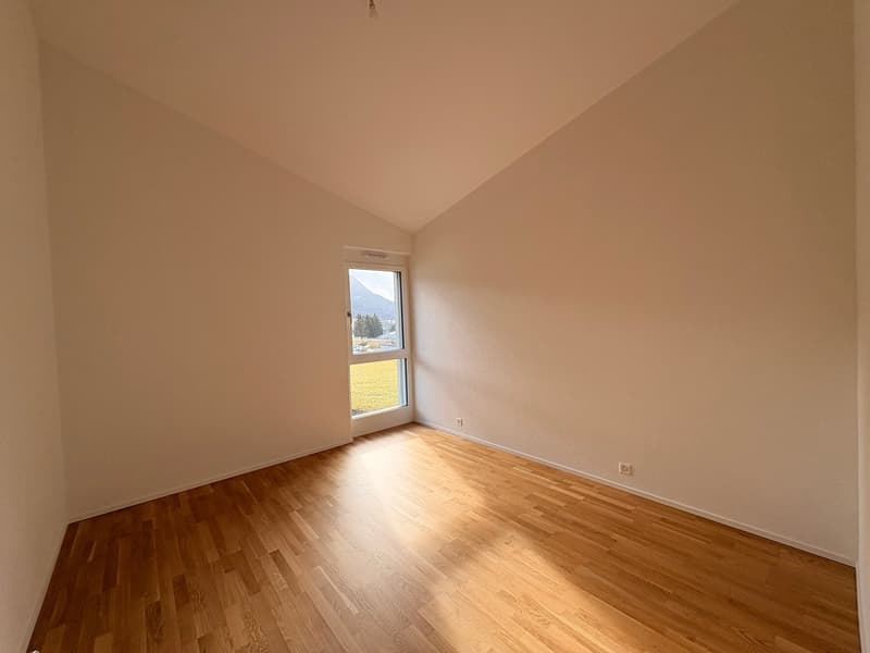 An empty room with wooden floors, white walls, a glass door, a window, and two power outlets.