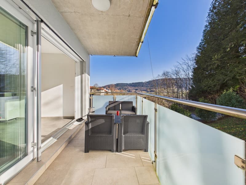 modern balcony with glass railings, outdoor seating, table with a red cup, and a scenic view