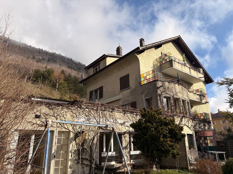 2 story house, beige exterior, multiple balconies, surrounded by trees, mountain in the background